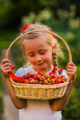 girl with eyes closed admires ripe strawberries from basket
