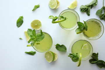 Fresh home-made healthy lemonade with lemon, lime and mint in a glass on white background and ingredients laying on the table