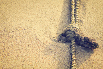 Mooring rope with knots on fine sand in morning (vintage concept style)
