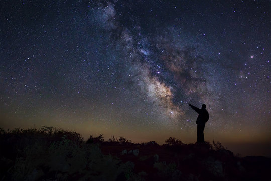 A Man is standing next to the milky way galaxy pointing on a bri
