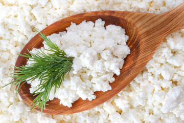 crumbly cottage cheese in the wooden spoon with dill on the top - 115854524