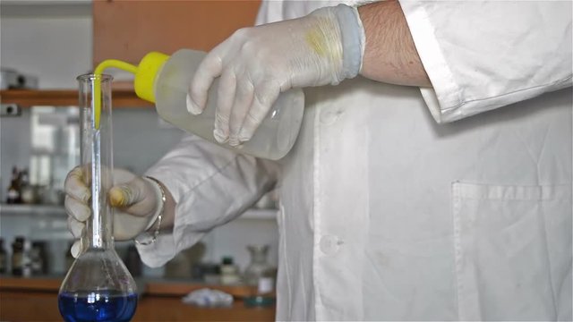Close-up hands in gloves of the lab tehnician in the white coat dilution blue liquids in the laboratory experiment.