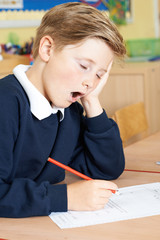 Male Elementary School Pupil Yawning In Classroom