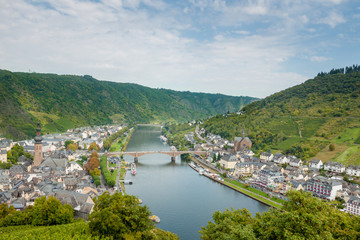 Fototapeta na wymiar The picturesque German town of Cochem from above. Germany. Urban landscape with river and bridge. The town is surrounded by vineyards. Blue sky and white clouds. Old town.