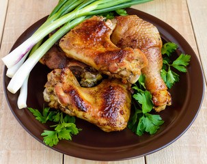 Roasted juicy chicken (legs, winglets) on a clay plate on a light wooden background. The top view