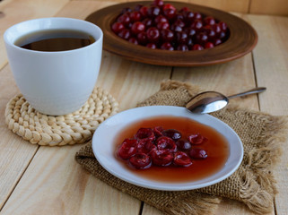 Cherry jam and a cup of tea on a light wooden background.