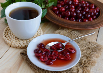 Cherry jam and a cup of tea on a light wooden background. The top view