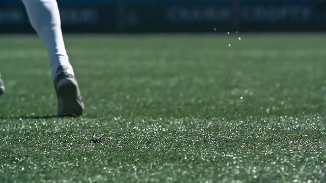 Legs of soccer player running and kicking a ball on green wet grass in slow motion