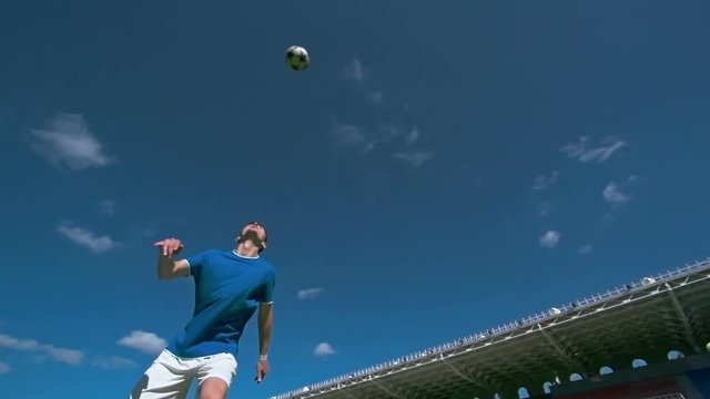 Low angle view of young professional soccer player tossing a ball, kicking it in the air and falling in slow motion