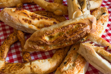 The composition of bread. French baguette with cheese, homemade bun with bacon, white bread with mushrooms, white bread with cheese and pretzel on the tablecloth