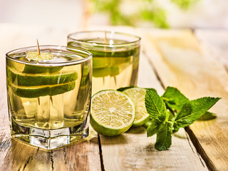 Alcohol drink. On wooden boards two glasses with alcohol green transparent drink. A drink number hundred sixty five mojito cocktail with half lime and mint . Country life style. Light background.