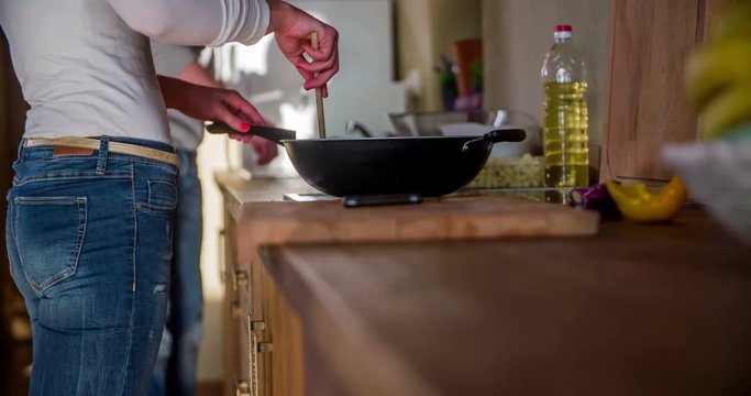 A young lady is preparing some dinner for her and her boyfriend. She is stirring vegetables in the wook with the wooden spoon. Close-up shot.
