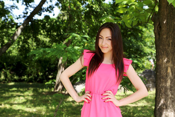 Fototapeta premium Young beautiful woman in pink dress standing in the park