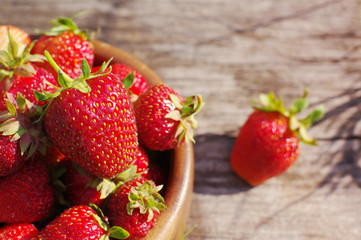 Fresh juicy berries of strawberry in a wooden plate on a wooden old surface. 