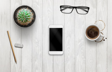 Smart phone mockup on white wooden desk. Coffee, plant, glasses beside.