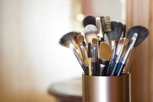 Makeup brushes in metal stand over blurred abstract room background