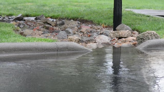 Rain flowing down an urban street into a stormwater curb and drain system