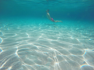 Young beard man with glasses diving in a blue clean water