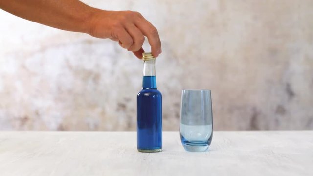 Mann sch&uuml;ttet blau eingef&auml;rbtes Wasser aus Flasche in ein Glas