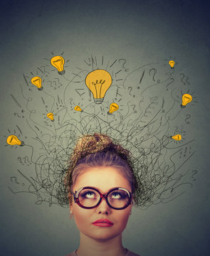 thinking woman in glasses with question signs and light idea bulb above head looking up wondering