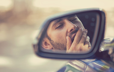 Fototapeta na wymiar Side mirror view sleepy tired yawning man driving car after long hour drive