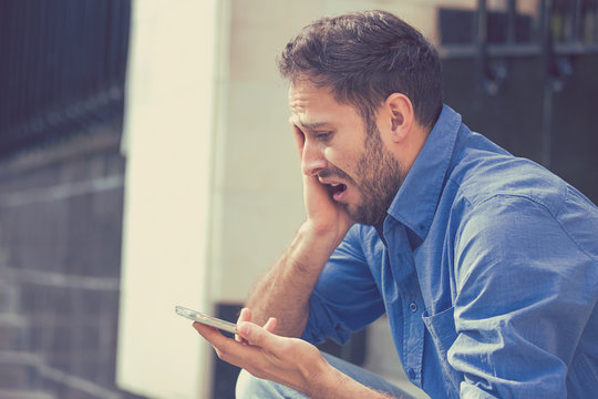 Desperate sad young man looking at bad text message on his mobile phone