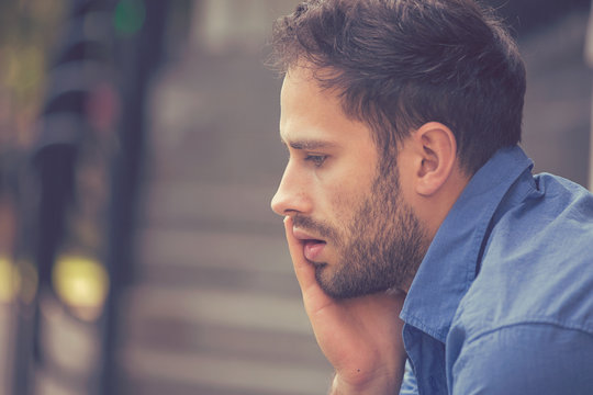 side profile sad depressed stressed young businessman sitting outside corporate office