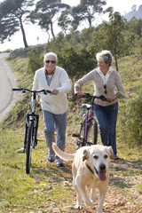 couple de sénior souriant se baladant en vélo avec leur chien