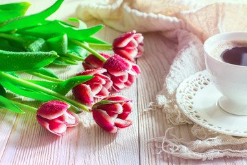 Red flowers tulips and cuf of coffee on light backgroung. Morning light.