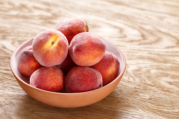 Ripe peaches in bowl on wooden background
