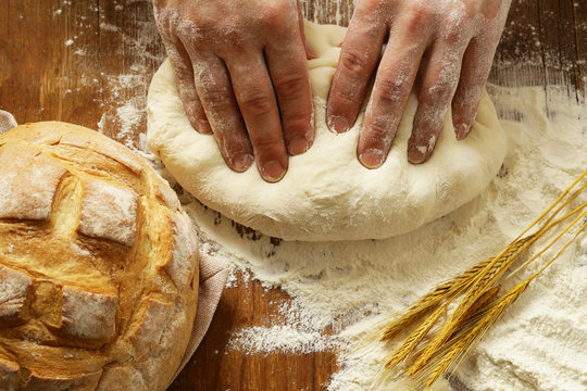 Chef hands with dough and homemade natural organic bread and flour on a wooden background