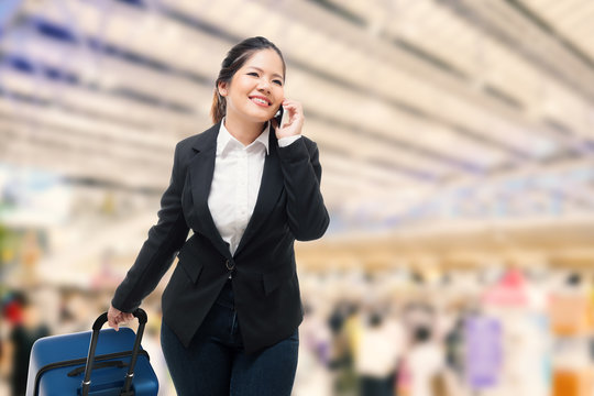 businesswoman talking on mobile phone while carrying luggage in airport