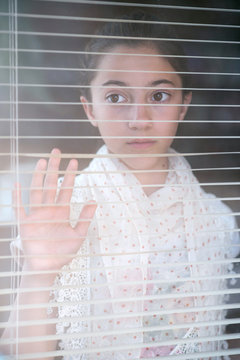 Girl looking through persian blinds on window