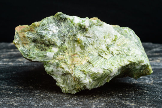 Large green diopside crystal on black slab of rock.