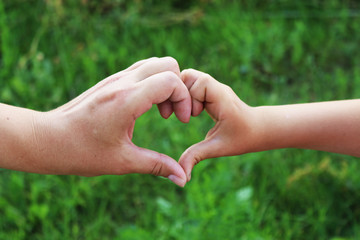 A mother and child made a heart with hands on dark background