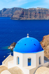 View of famous church with blue dome against blue sea with caldera in Oia village, Santorini island, Greece