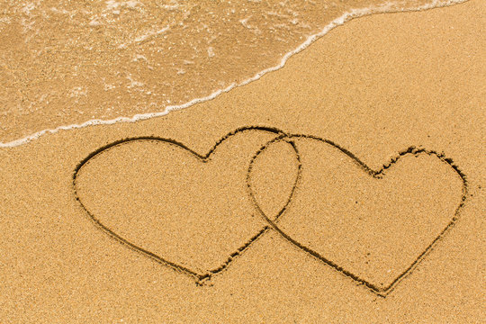 Two of hearts drawn on a sandy beach in the line of sea surf.
