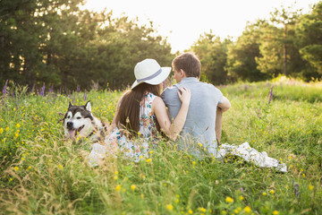 Naklejka na ściany i meble couple in love with a dog, Husky Malamute, sunset forest, woman in a cowboy hat