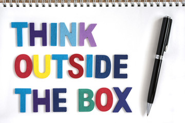 Colorful wood letters word think outside the box in open notebook with a pen Quotes business concept