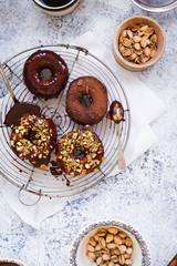 Chocolate donuts over cooling rack with pistachio nuts.