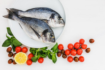 Two raw dorado fish on white plate with vegetables. Top view, copy space.