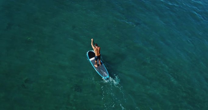 Aerial view of young man stand up paddle boarding on blue ocean waves