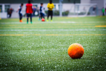 Dirty soccer ball on the artificial turf field with game in the background - obrazy, fototapety, plakaty