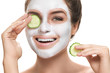 Woman with facial mask and cucumber slices in her hands