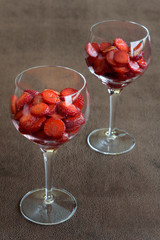 Sliced strawberries in wine glasses on a brown background

