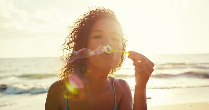 Beautiful young woman blowing bubbles on the beach at sunset, soft warm vintage color tone