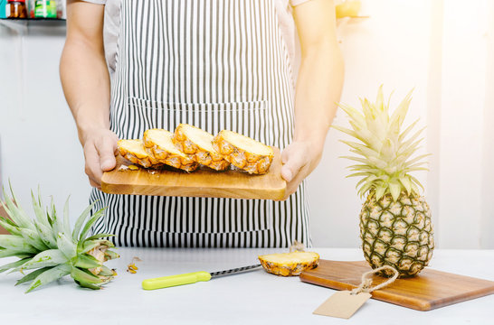 Hands holding ripe pineapple on chopping board.
