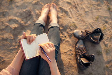 female makes notes and sitting on the beach;