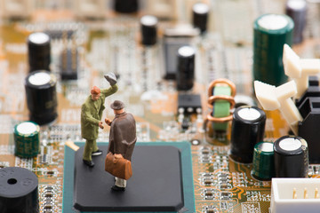 コンピューターの基盤の上で握手をしているミニチュア人物