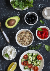 Quinoa, avocado, roasted peppers, fresh cucumbers and tomatoes, arugula, goat cheese - ingredients for salad. On a dark background, top view